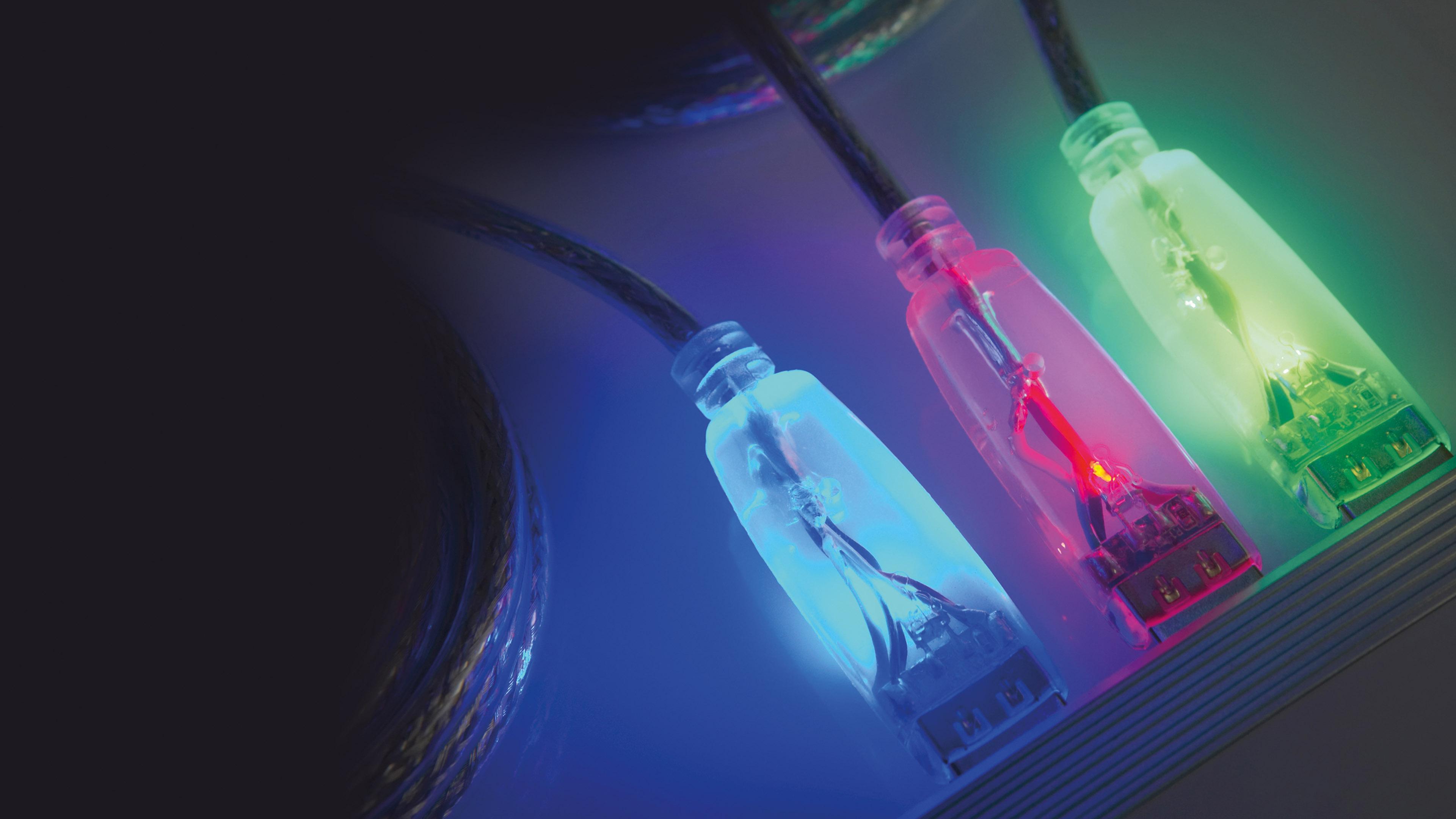 Leuchtende USB-Kabel in verschiedenen Farben (blau, rot, grün), die an ein elektronisches Gerät angeschlossen sind.