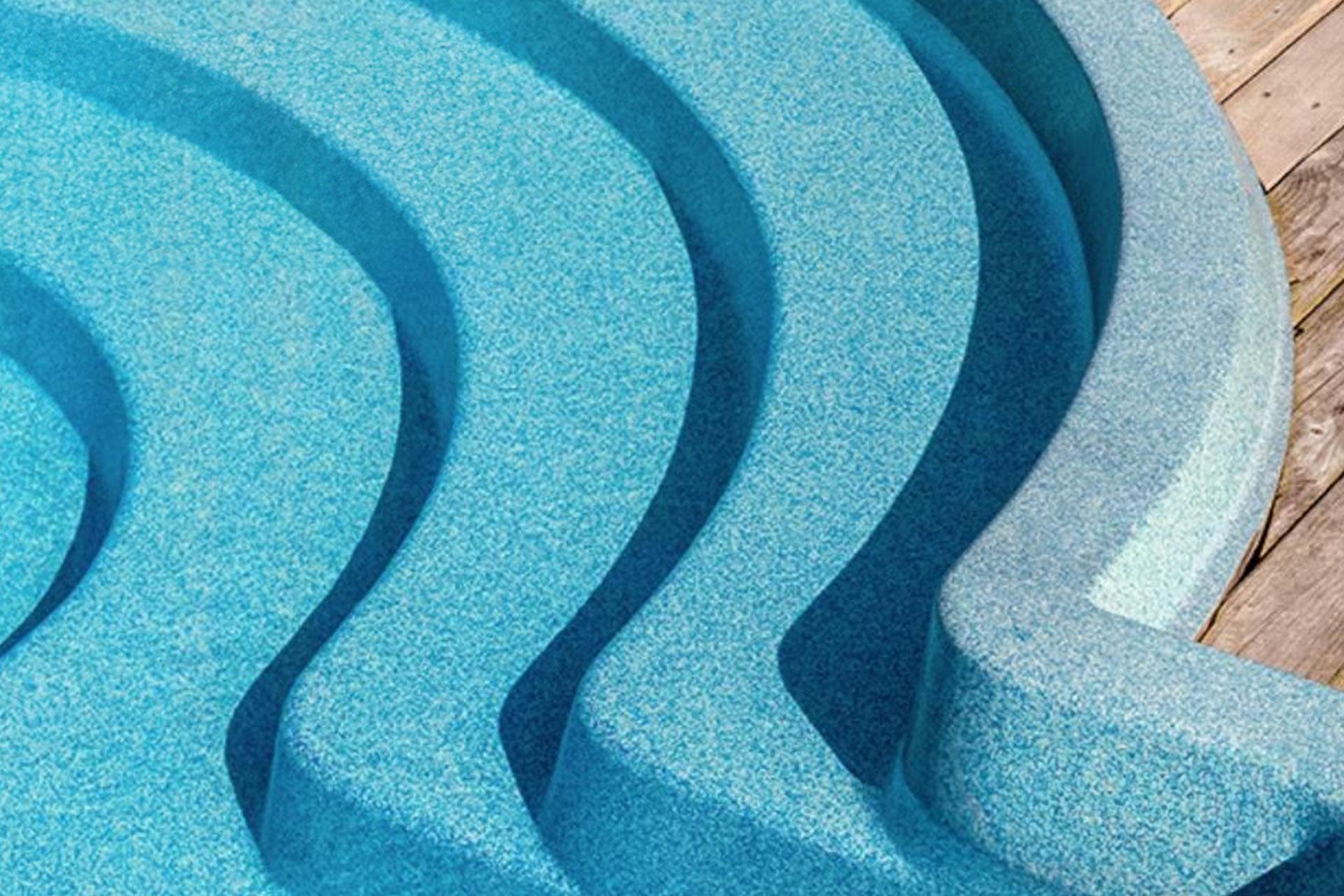 Detailaufnahme einer blauen, geschwungenen Pooltreppe, die in einen Pool führt, neben einem Holzdeck.