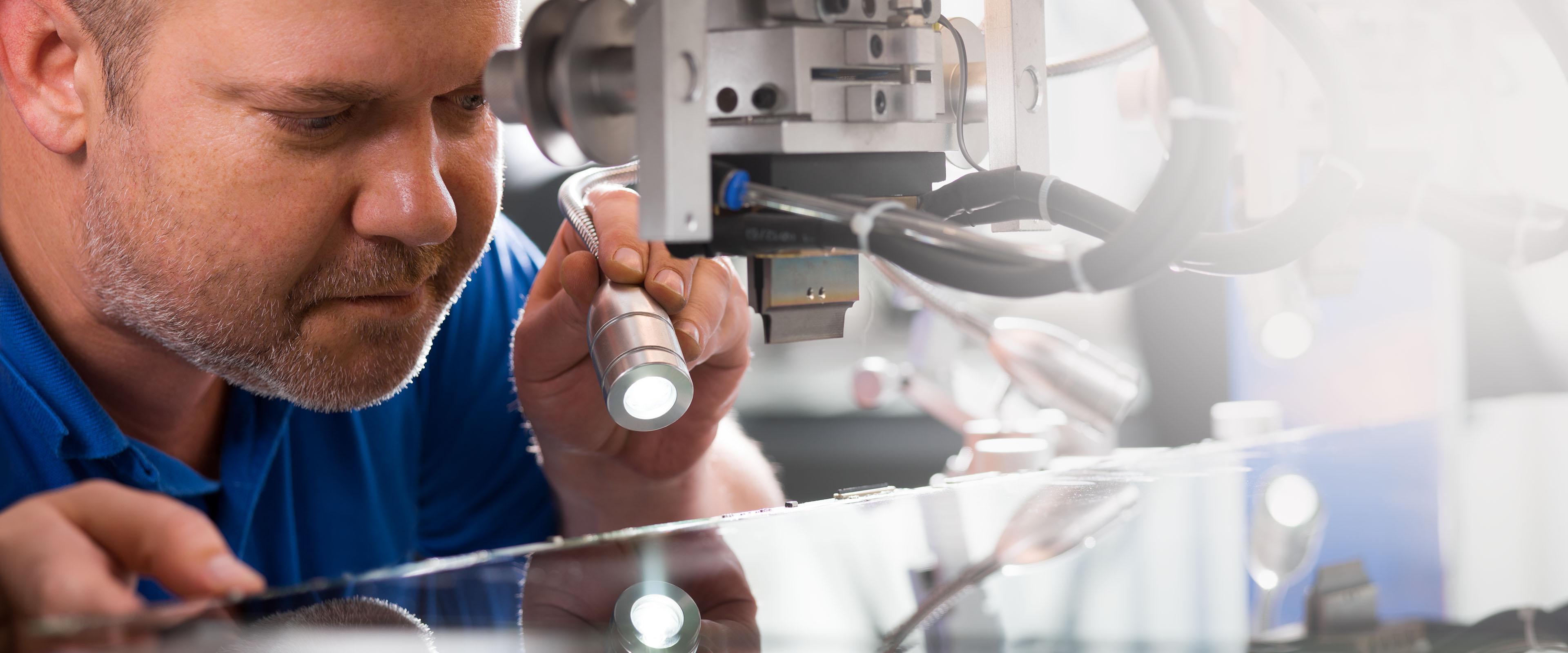 Techniker inspiziert eine Maschine mit einer Taschenlampe, konzentriert sich auf Details bei der Arbeit.