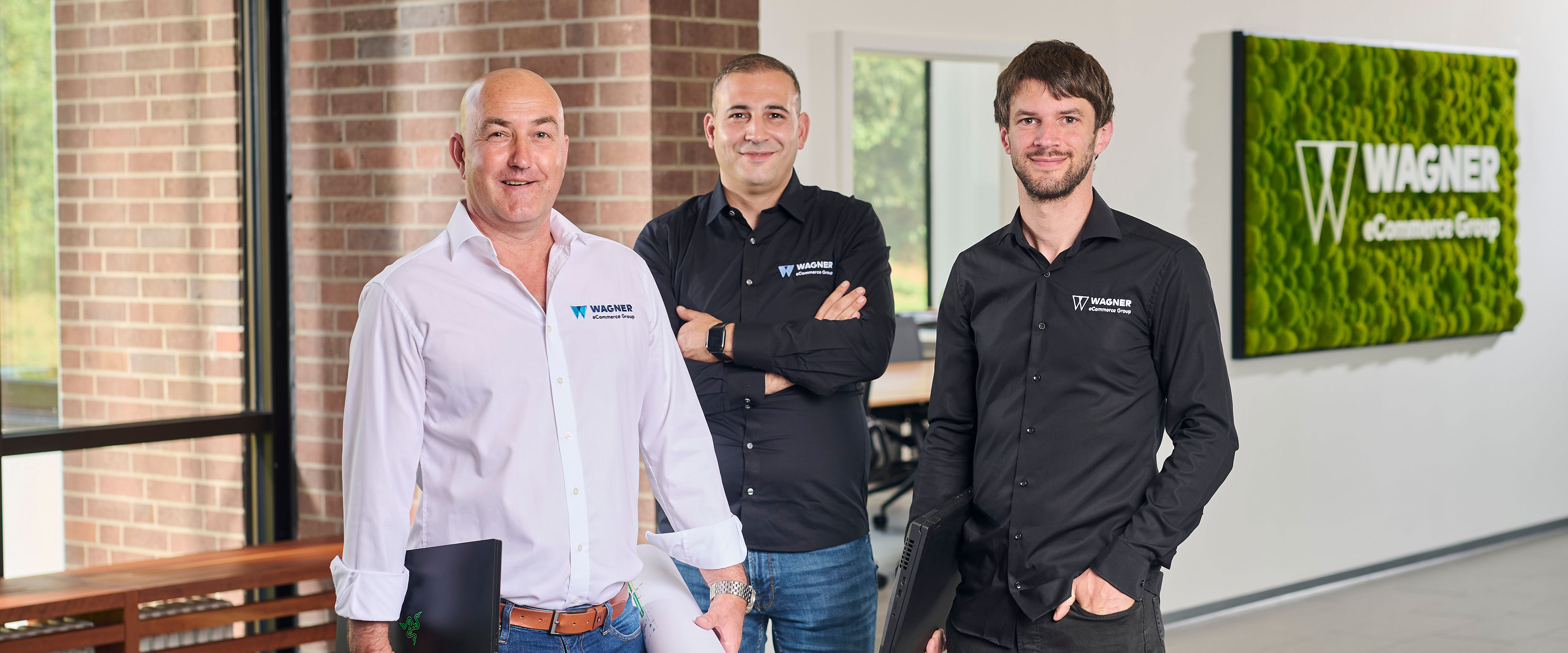 Fünf Personen stehen in einem Büro und halten jeweils eine Nummernkarte von 1 bis 4 in der Hand. Im Hintergrund ist ein Whiteboard mit Zahlen zu sehen. Das Büro ist modern gestaltet und hat eine grüne Pflanzenwand.