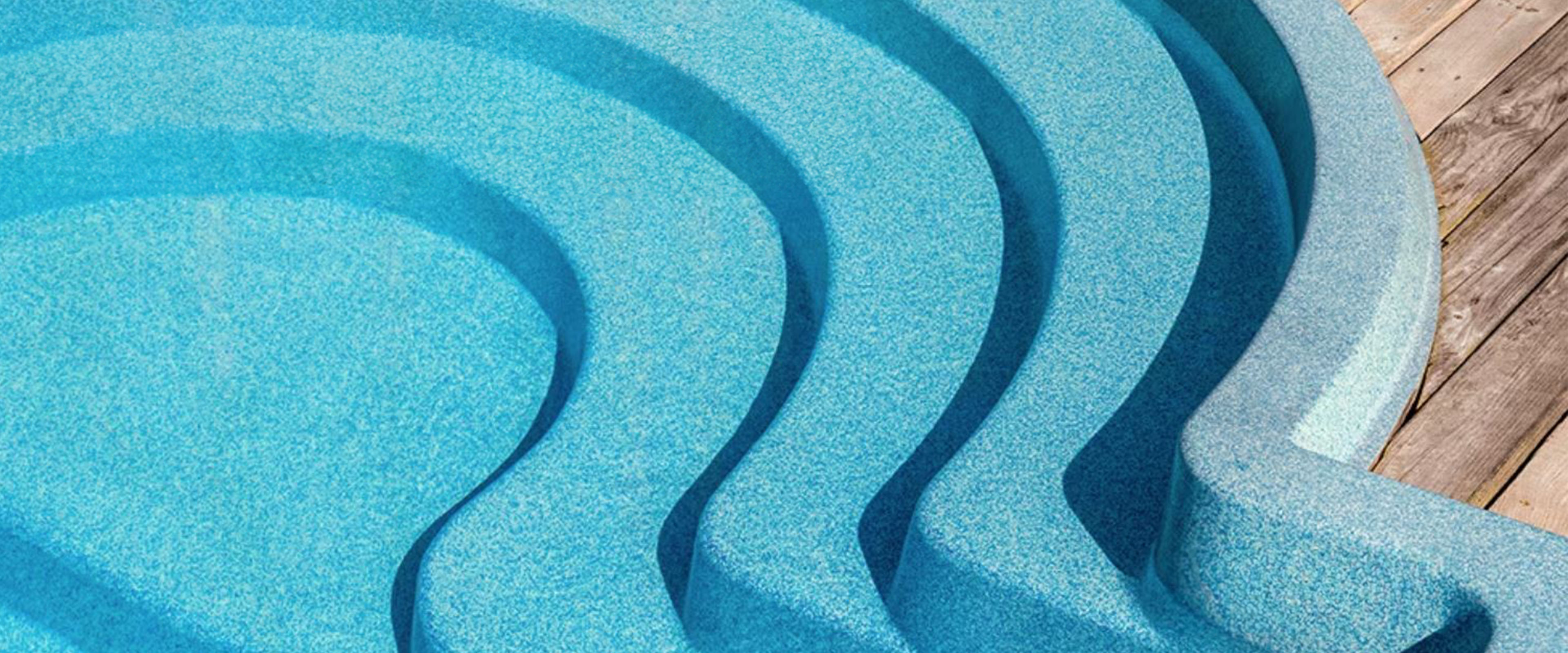 Detailaufnahme einer blauen, geschwungenen Pooltreppe, die in einen Pool führt, neben einem Holzdeck.