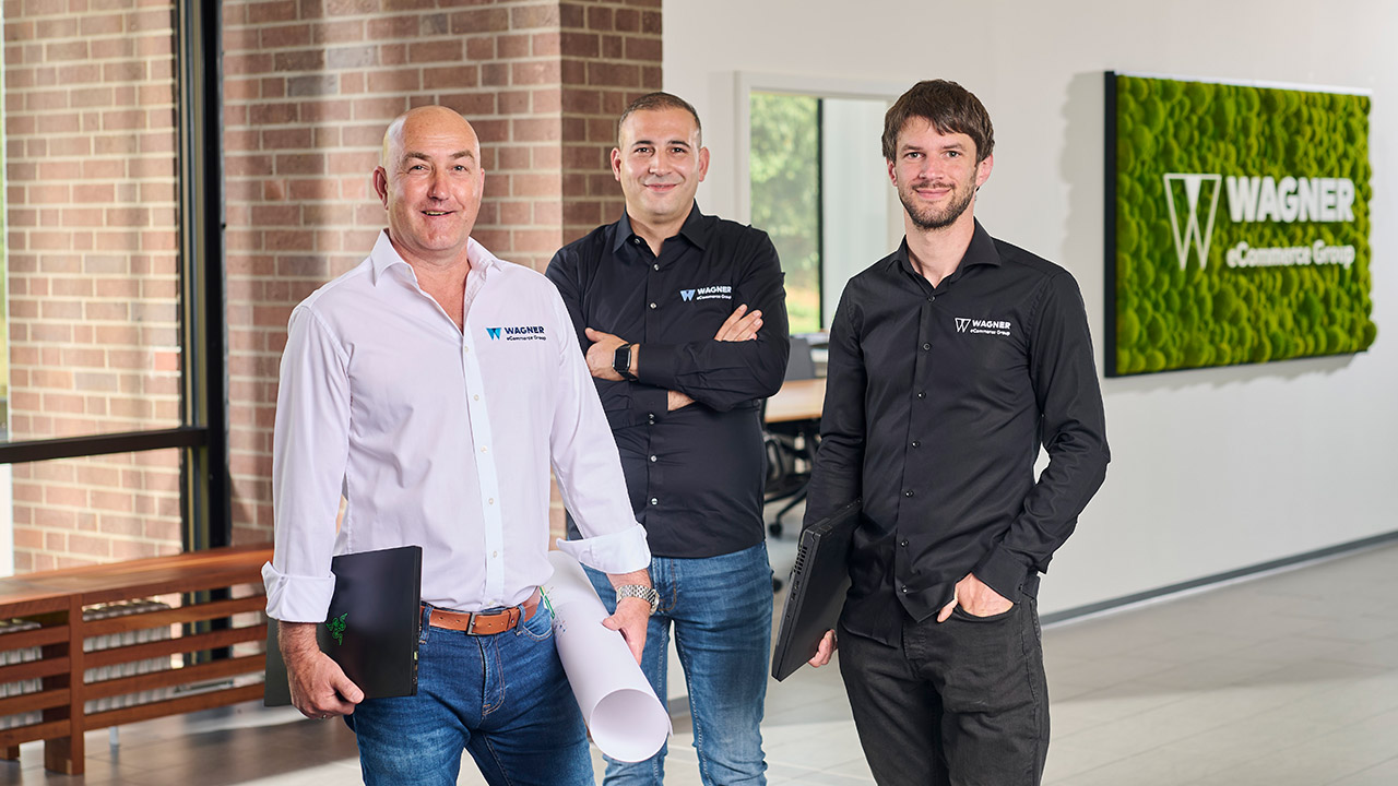 Fünf Personen stehen in einem Büro und halten jeweils eine Nummernkarte von 1 bis 4 in der Hand. Im Hintergrund ist ein Whiteboard mit Zahlen zu sehen. Das Büro ist modern gestaltet und hat eine grüne Pflanzenwand.
