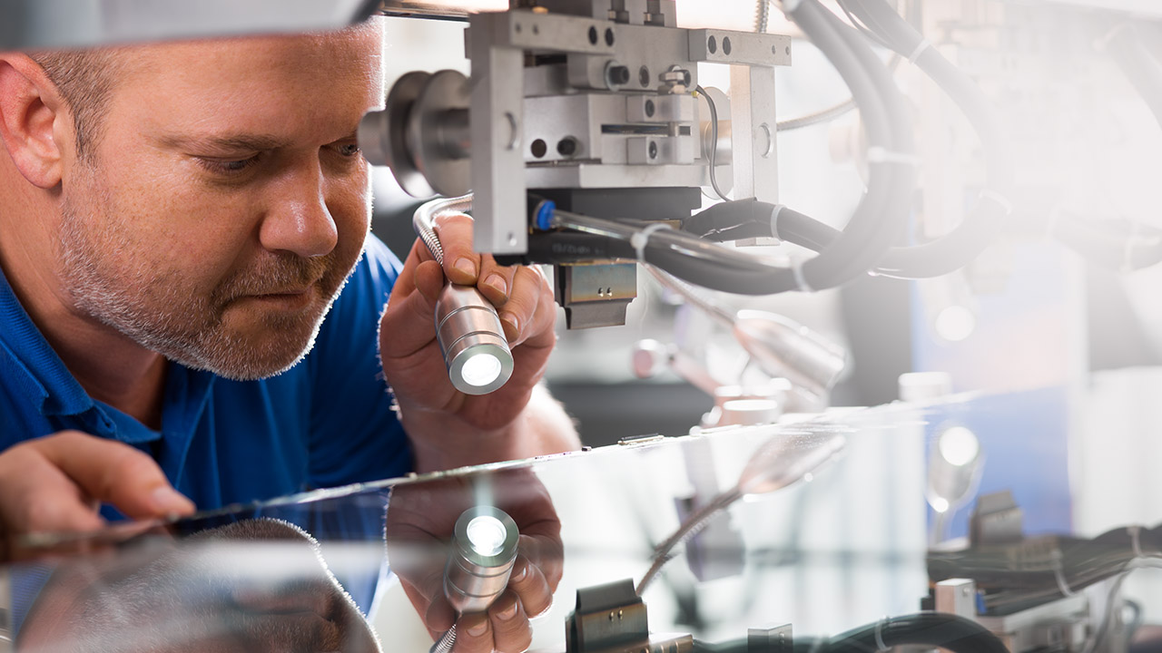 Techniker inspiziert eine Maschine mit einer Taschenlampe, konzentriert sich auf Details bei der Arbeit.