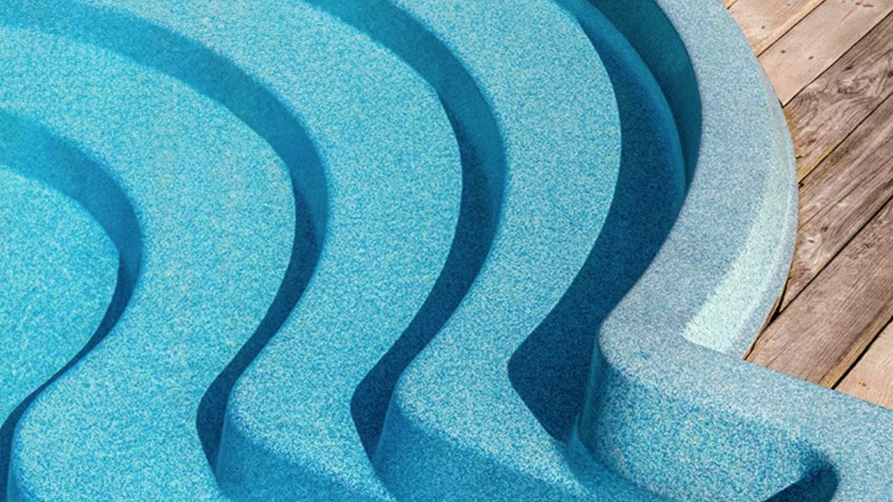 Detailaufnahme einer blauen, geschwungenen Pooltreppe, die in einen Pool führt, neben einem Holzdeck.