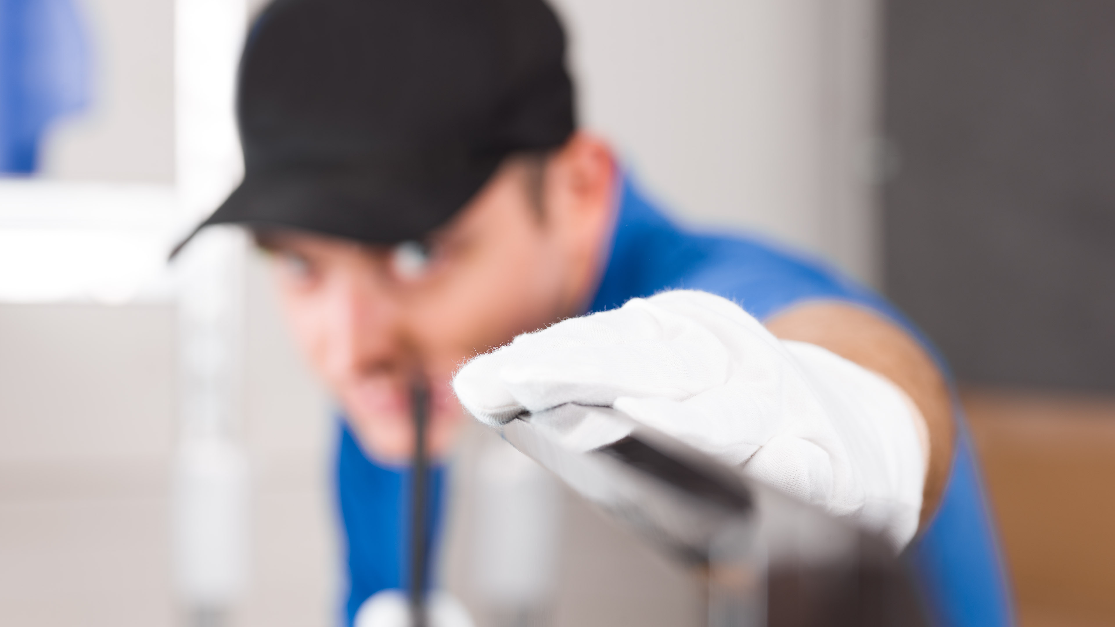 Handwerker im blauen Overall, unscharf im Hintergrund, trägt weiße Handschuhe und inspiziert sorgfältig ein Werkstück.